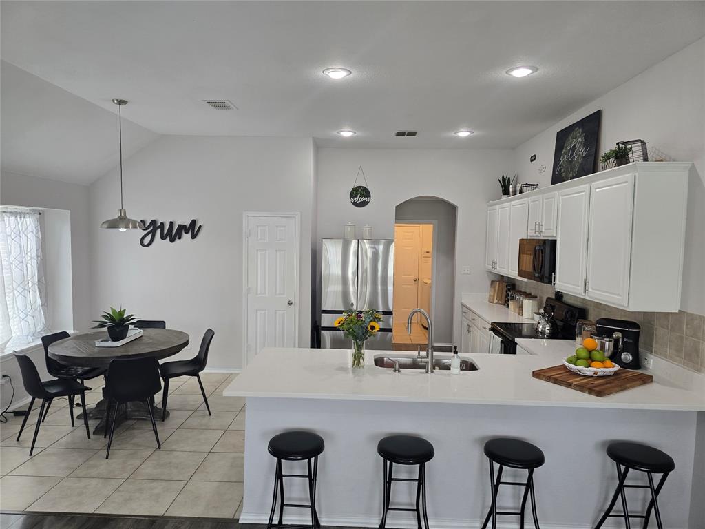 213 Arabian Road Waxahachie, TX 75165 - Photo 7 of 29 Kitchen featuring black appliances, a peninsula, a breakfast bar area, vaulted ceiling, and white cabinets