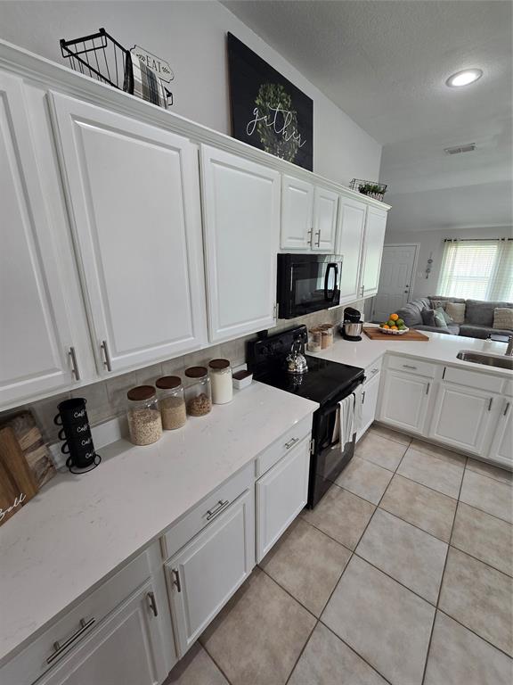 213 Arabian Road Waxahachie, TX 75165 - Photo 29 of 29 Kitchen with white cabinets, black appliances, open floor plan, light tile patterned floors, and light stone counters