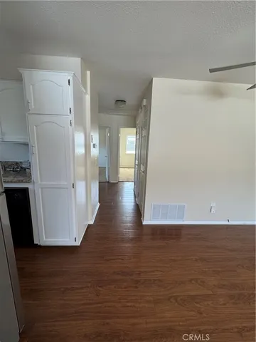 a view of a refrigerator in kitchen and an empty room with wooden floor
