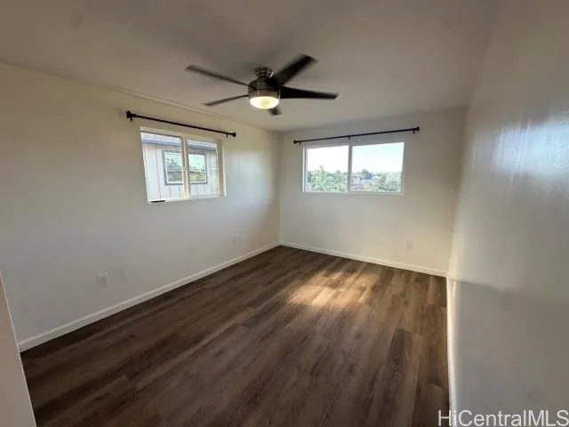 an empty room with wooden floor ceiling fan and windows