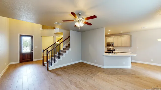 a view of an empty room with wooden floor and a ceiling fan