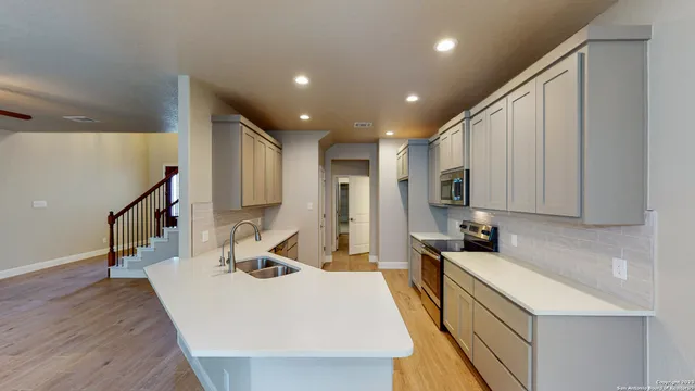 a large kitchen with stainless steel appliances a large counter top a stove a sink a refrigerator and a cabinets