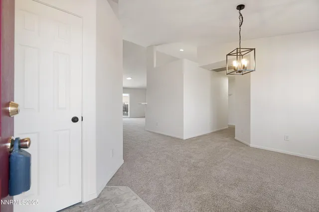 an empty room with chandelier fan and kitchen view