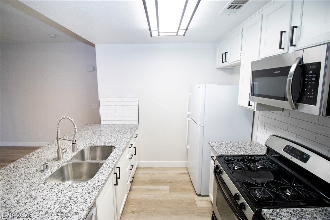 1468 Reef Ridge Court Las Vegas, NV 89128 - Photo 4 of 22 A galley kitchen showcasing pristine granite countertops, a double basin sink, and stainless steel appliances.