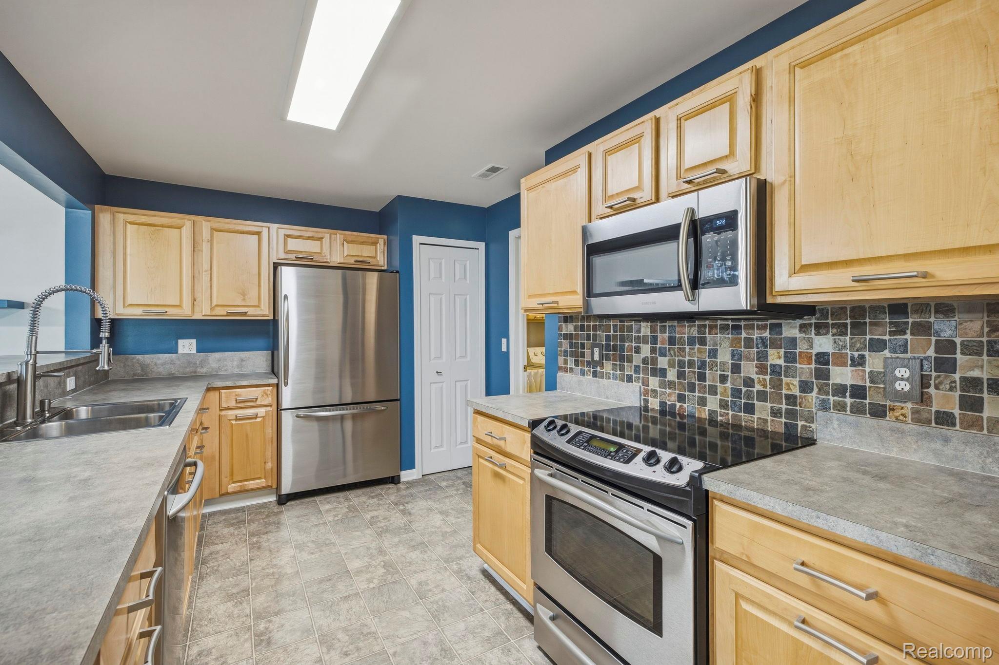 1905 Flagstone Circle Rochester, MI 48307 - Photo 17 of 33 Stainless steel appliances, light wood-finish cabinetry, tile flooring, mosaic tile backsplash, and light-toned countertops