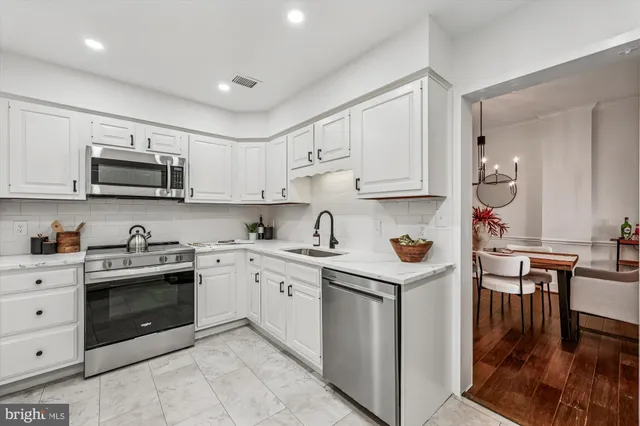 a kitchen with stainless steel appliances granite countertop a stove top oven a sink dishwasher and white cabinets with wooden floor