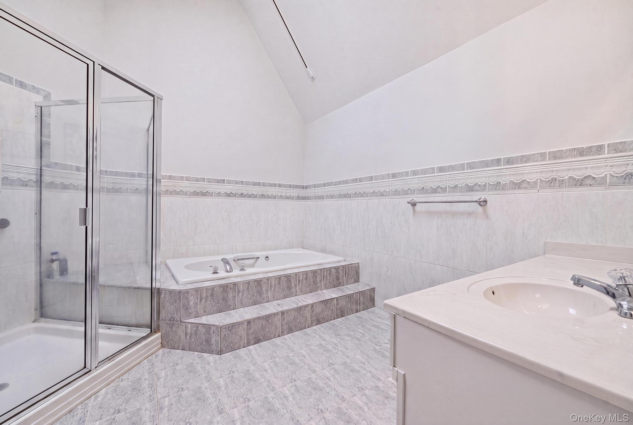 19 Sunset Road West Albertson, NY 11507 - Photo 13 of 24 Spacious bathroom featuring a glass-enclosed shower, a stepped platform tub, a single vanity with an integrated sink, tiled walls, and tiled flooring