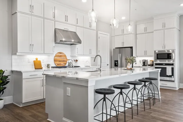 a kitchen with stainless steel appliances granite countertop a sink a stove a refrigerator and a dining table with wooden floor