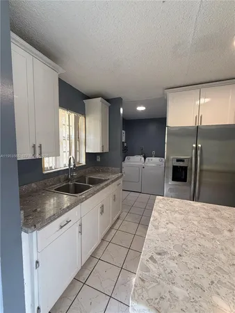 a large kitchen with granite countertop a sink and white cabinets