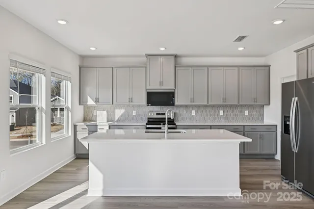 a white kitchen with stainless steel appliances granite countertop a stove a sink a refrigerator and white cabinets