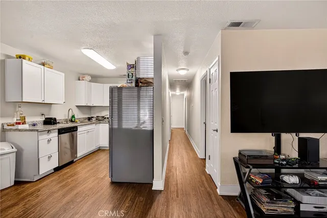 a living room with stainless steel appliances a dining table wooden floor and a view of kitchen