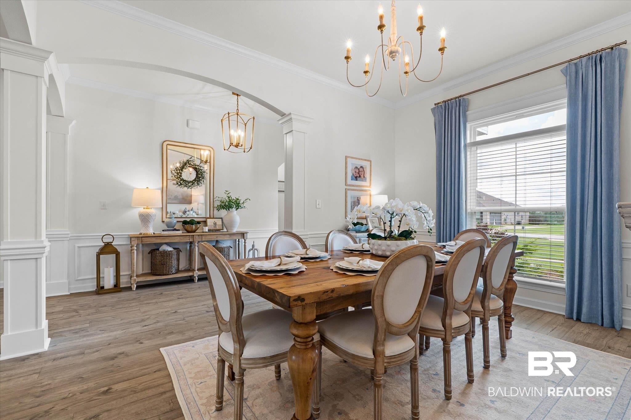 9074 Moses Way Theodore, AL 36582 - Photo 9 of 52 Dining area featuring a classic chandelier, wood-finish flooring, architectural archways, and detailed wainscoting