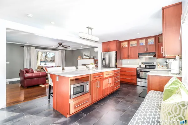 a large white kitchen with stainless steel appliances granite countertop a stove and a view of living room