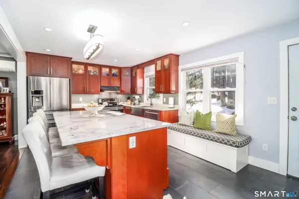 a room with stainless steel appliances kitchen island granite countertop a refrigerator a stove and a dining table with wooden floor