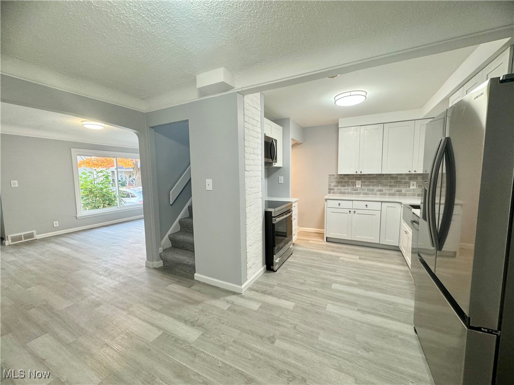 1215 Avondale Road Cleveland, OH 44121 - Photo 10 of 27 Kitchen with light wood-type flooring, a textured ceiling, white cabinetry, stainless steel appliances, and decorative backsplash