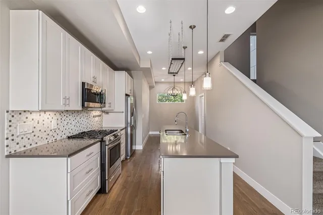 a kitchen with stainless steel appliances granite countertop a refrigerator a sink a stove and white cabinets with wooden floor