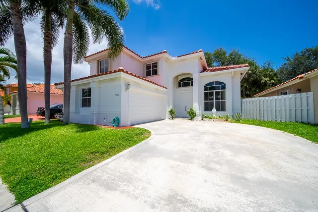 a view of a white house with a small yard and palm trees