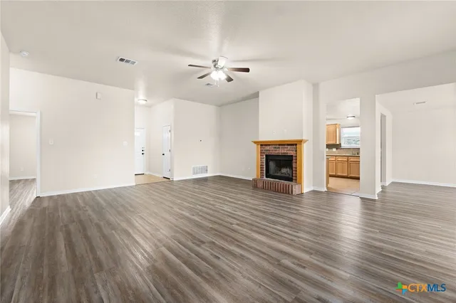 an empty room with wooden floor fireplace and windows