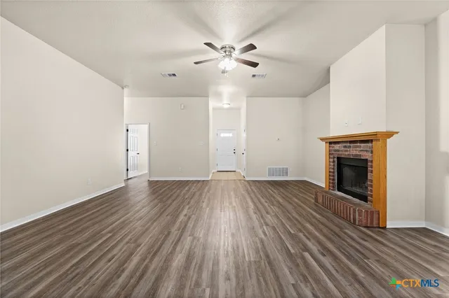 an empty room with wooden floor fireplace and windows