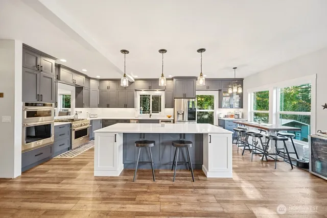 a kitchen with stainless steel appliances kitchen island granite countertop a refrigerator a stove and a wooden floors