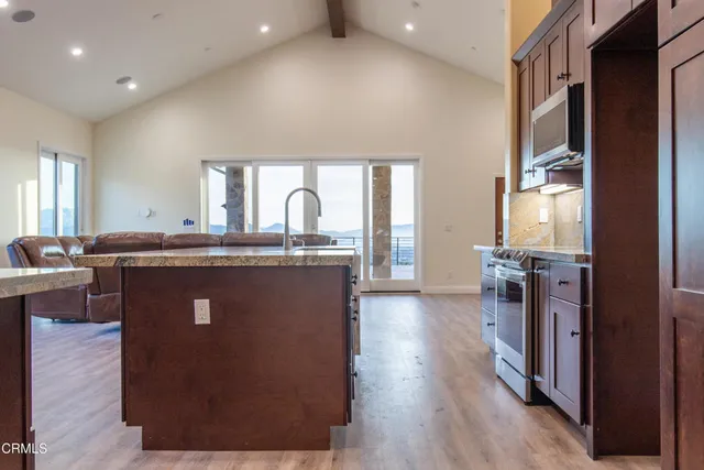 a kitchen with stainless steel appliances granite countertop a refrigerator a sink dishwasher a stove and a dining table with wooden floor