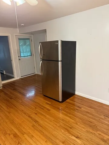 a view of an empty room with wooden floor and a refrigerator
