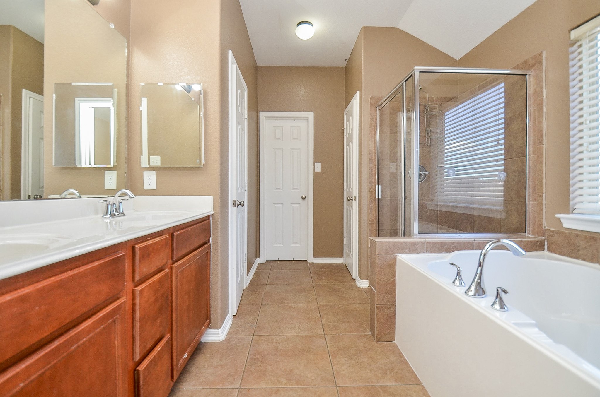 5411 Rio Drive Baytown, TX 77521 - Photo 24 of 30 The primary bathroom features a double vanity with wooden cabinetry, a glass-enclosed shower, and a large soaking tub with modern chrome fixtures that sits beneath a sunlit window creating the perfect place to relax and unwind.