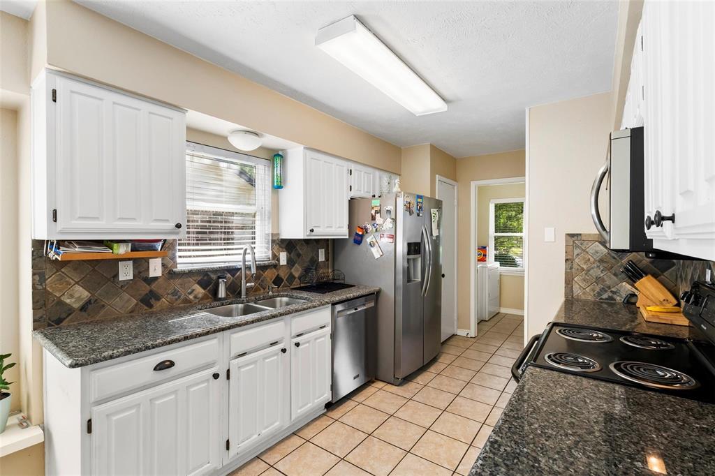 9212 Shipman Street Rowlett, TX 75088 - Photo 9 of 34 Kitchen featuring white cabinetry, stainless steel double sink, granite countertops with stone tile backsplash, stainless steel appliances and light tile patterned floors