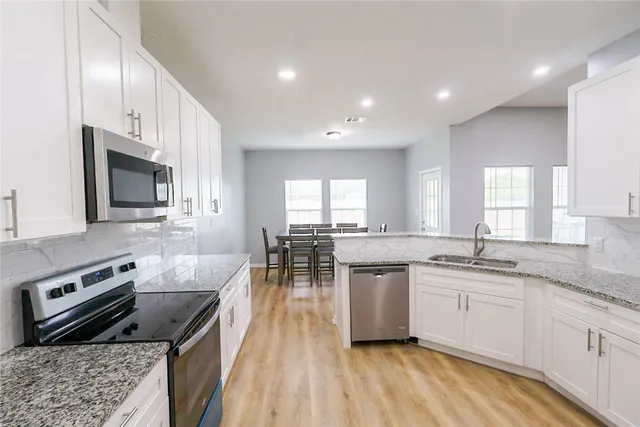 a kitchen with stainless steel appliances granite countertop a stove top oven a sink dishwasher a dining table and chairs with wooden floor