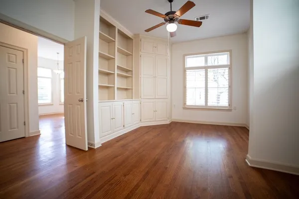 an empty room with wooden floor chandelier fan and windows