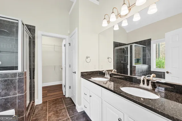 a spacious bathroom with a granite countertop double vanity sink a mirror and a shower