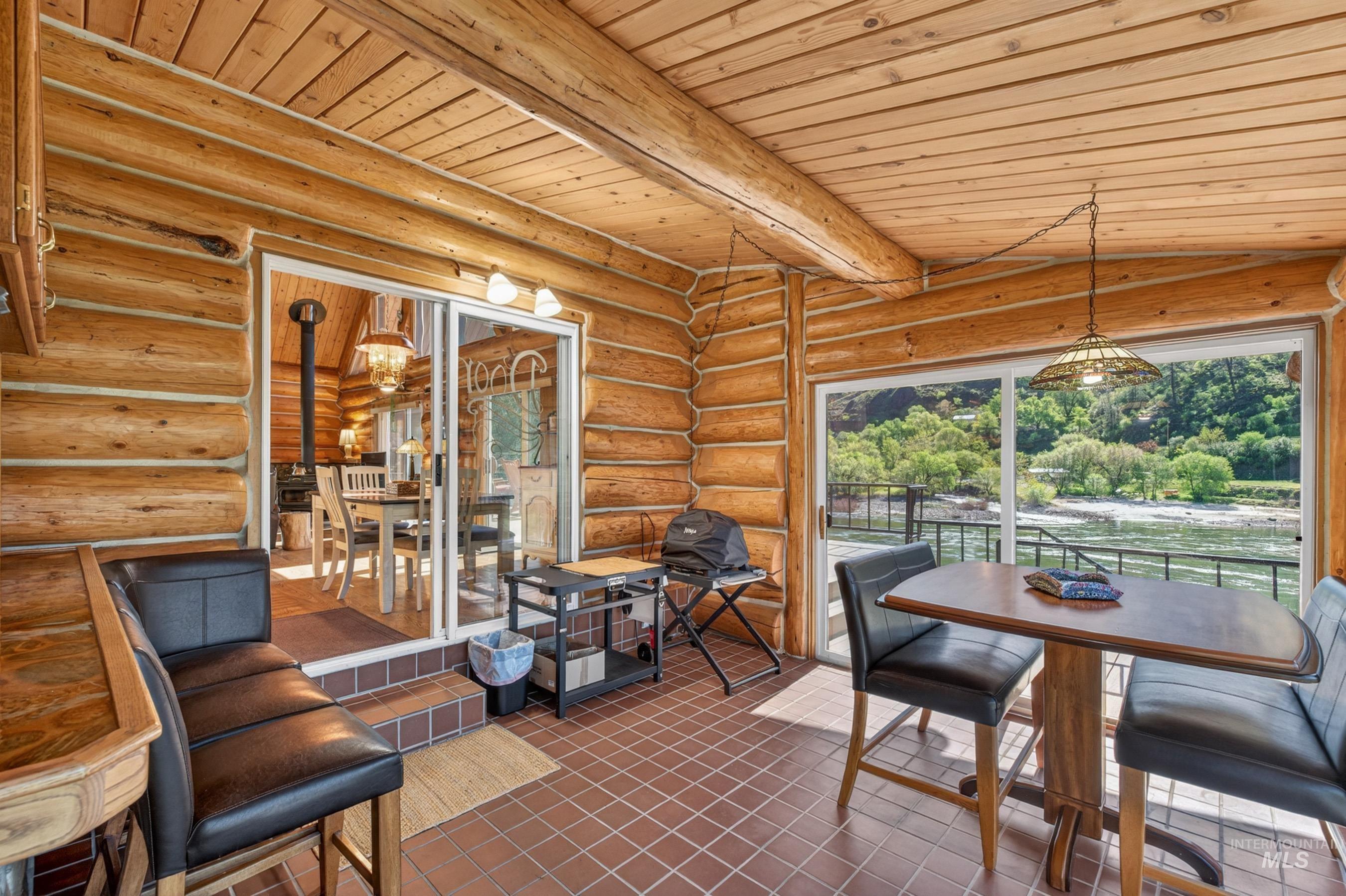 215 Doumecq Road White Bird, ID 83554 - Photo 13 of 50 Enclosed patio featuring log-style walls and ceiling, a tiled floor, and expansive sliding glass doors overlooking a river and lush hillside