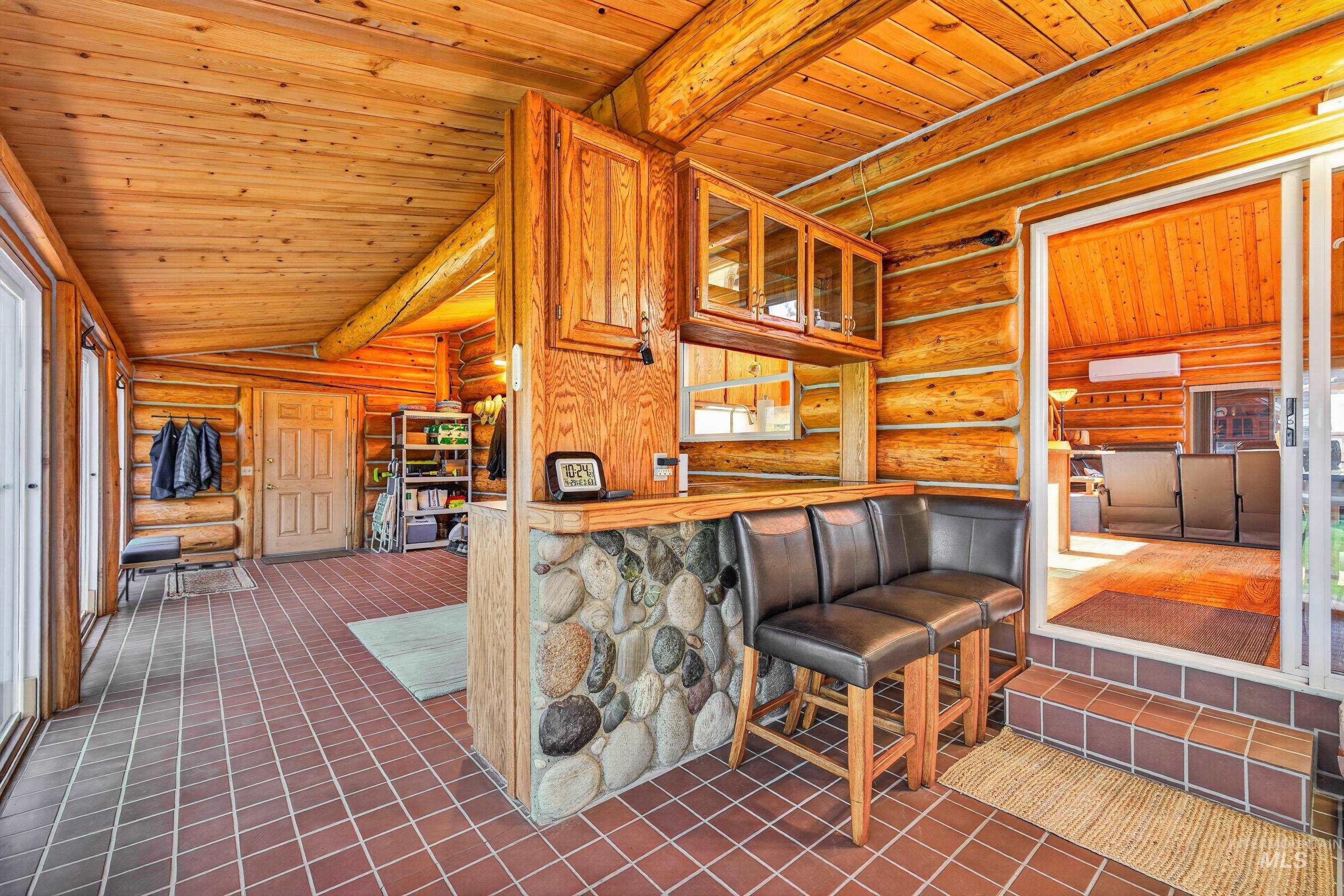 215 Doumecq Road White Bird, ID 83554 - Photo 14 of 50 Interior log cabin features natural wood walls and ceilings, red square tile flooring, a stone-faced bar with wood cabinetry and glass inserts, and a sliding glass door