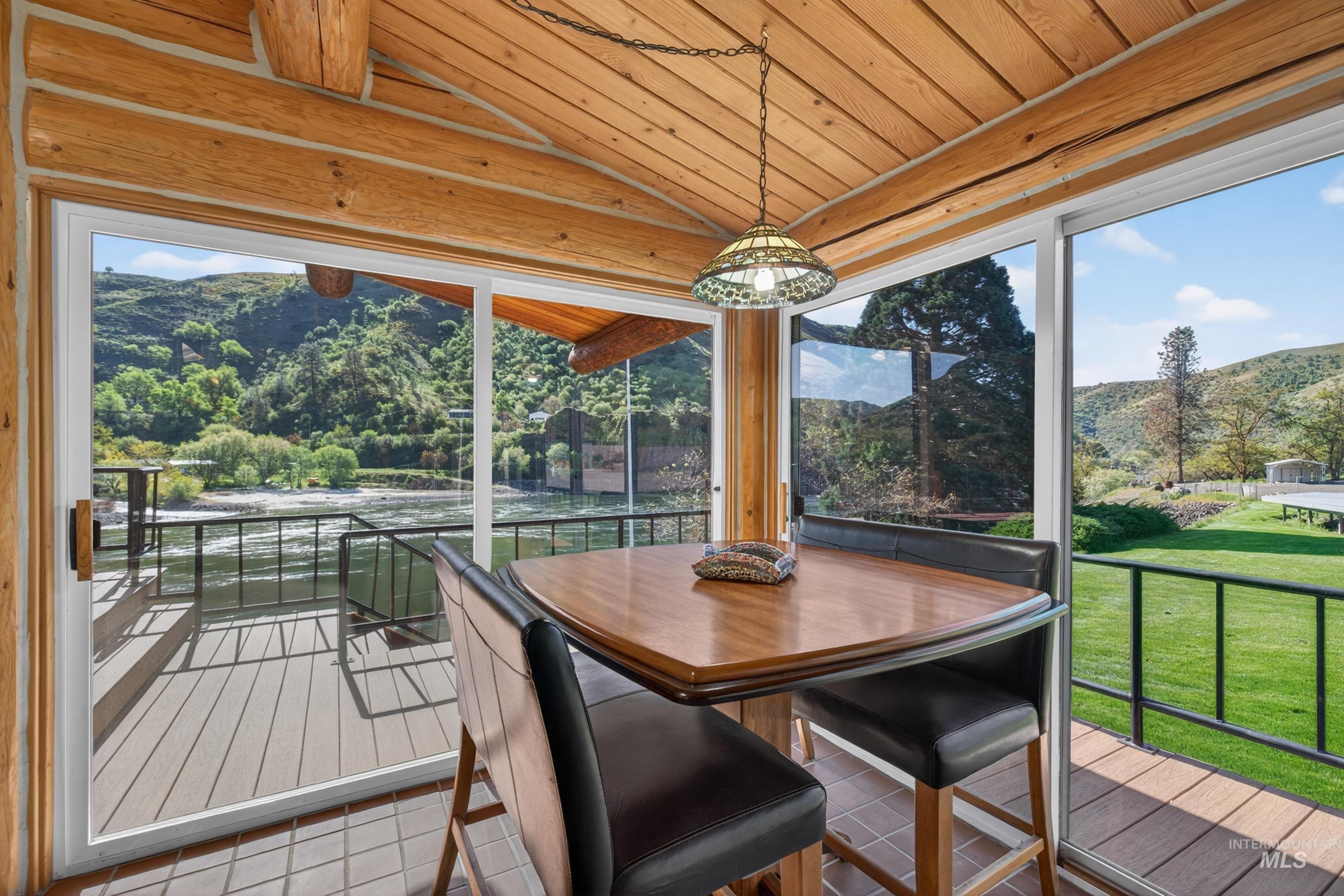 215 Doumecq Road White Bird, ID 83554 - Photo 15 of 50 Wood-paneled sunroom featuring exposed log beams, panoramic windows, tile flooring, and direct access to an outdoor deck