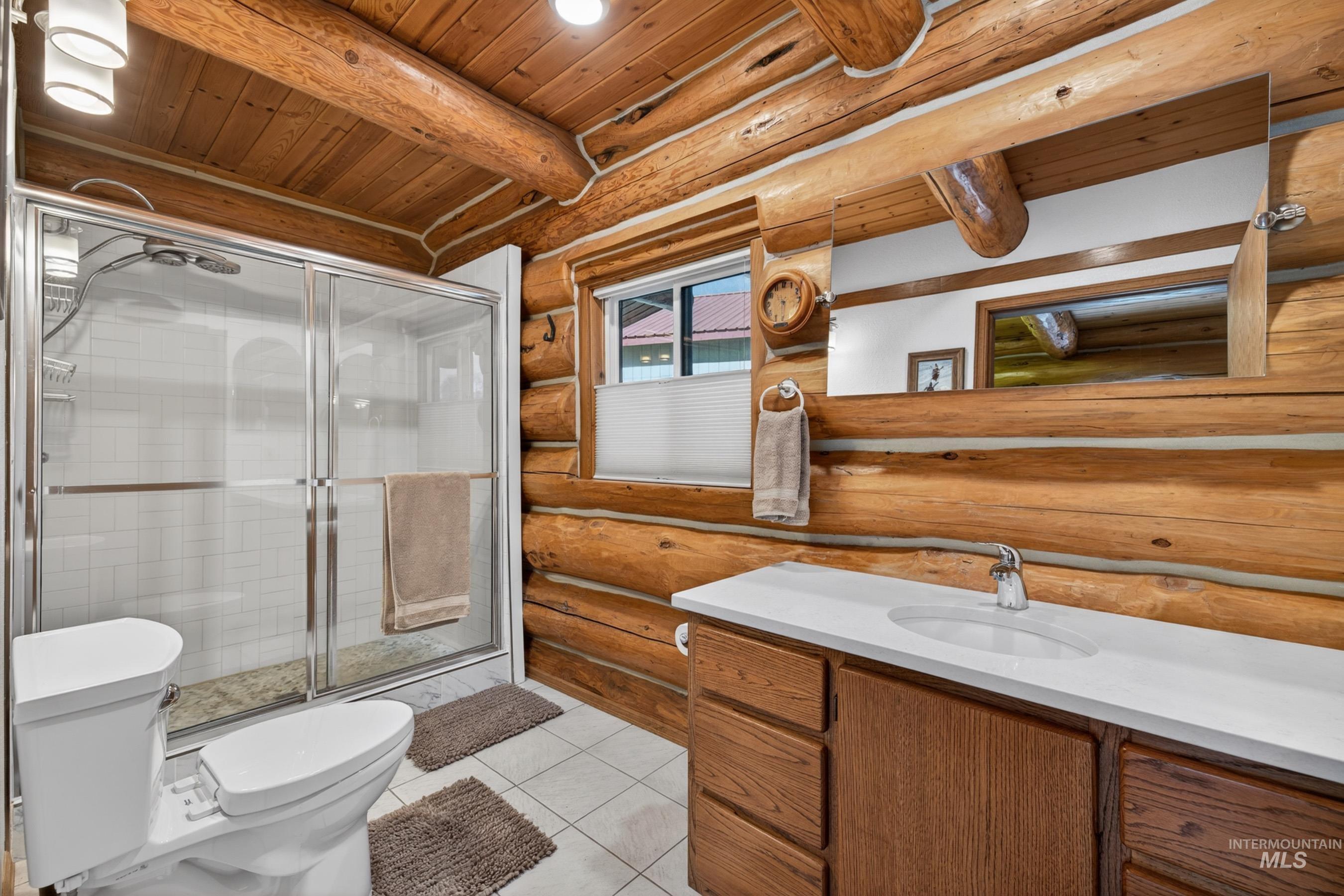 215 Doumecq Road White Bird, ID 83554 - Photo 19 of 50 Bathroom featuring natural log walls and ceiling, a white tile floor, a glass-enclosed shower with white subway tile, a vanity with wood-finish cabinetry, and a white countertop with an integrated sink