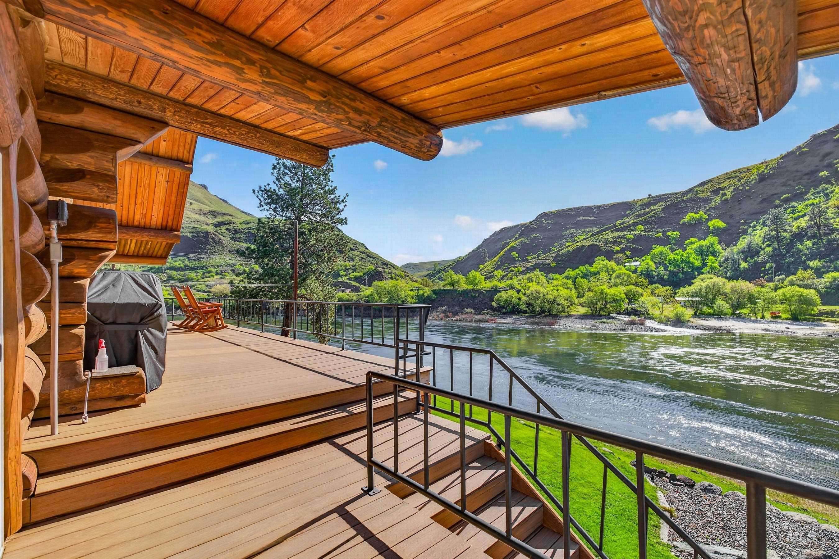 215 Doumecq Road White Bird, ID 83554 - Photo 37 of 50 Expansive wood-finish deck with black metal railings, overlooking a wide river and lush green hillsides