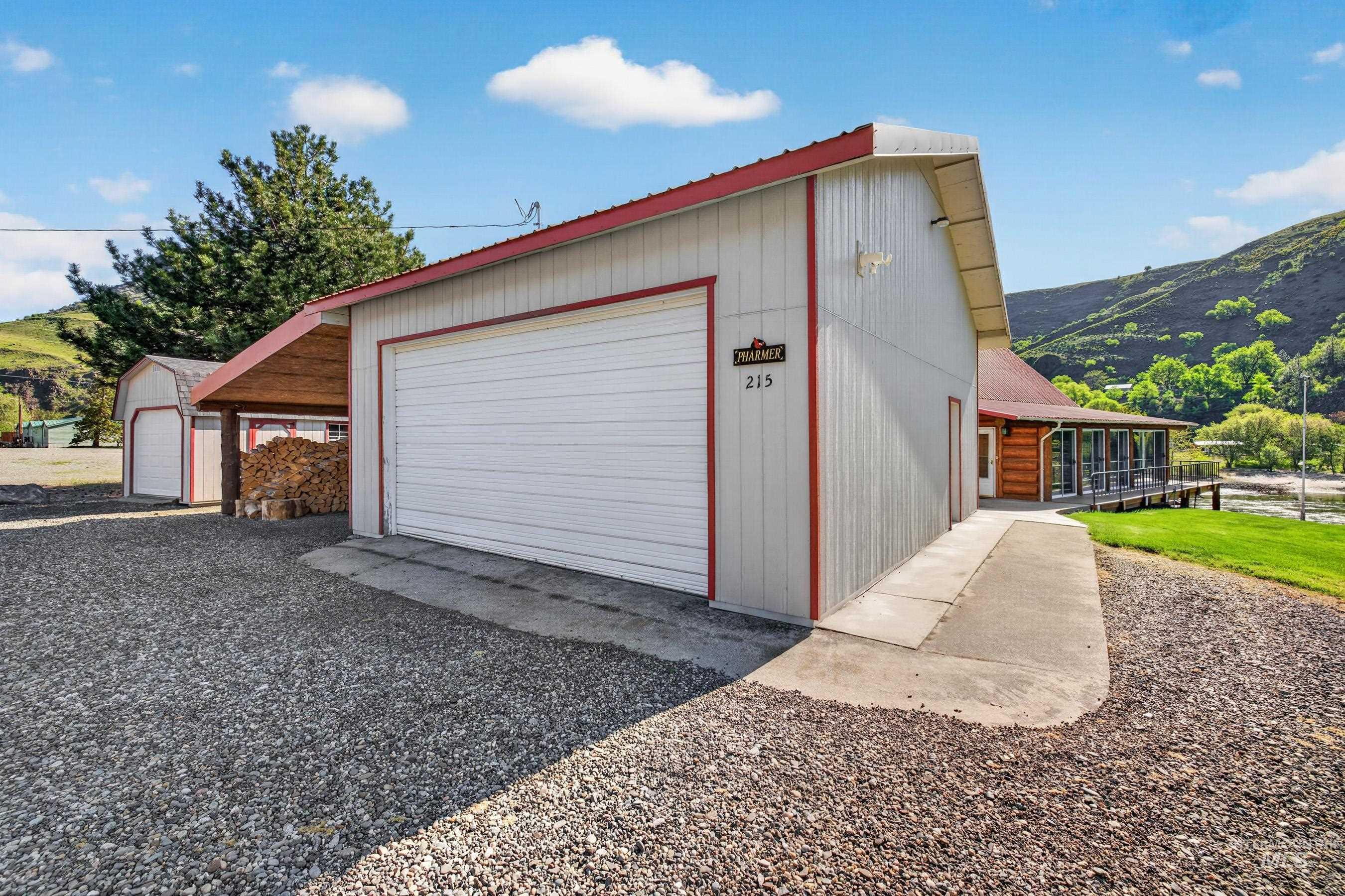 215 Doumecq Road White Bird, ID 83554 - Photo 41 of 50 Detached garage with white overhead door and red trim, featuring an adjacent carport with wood storage