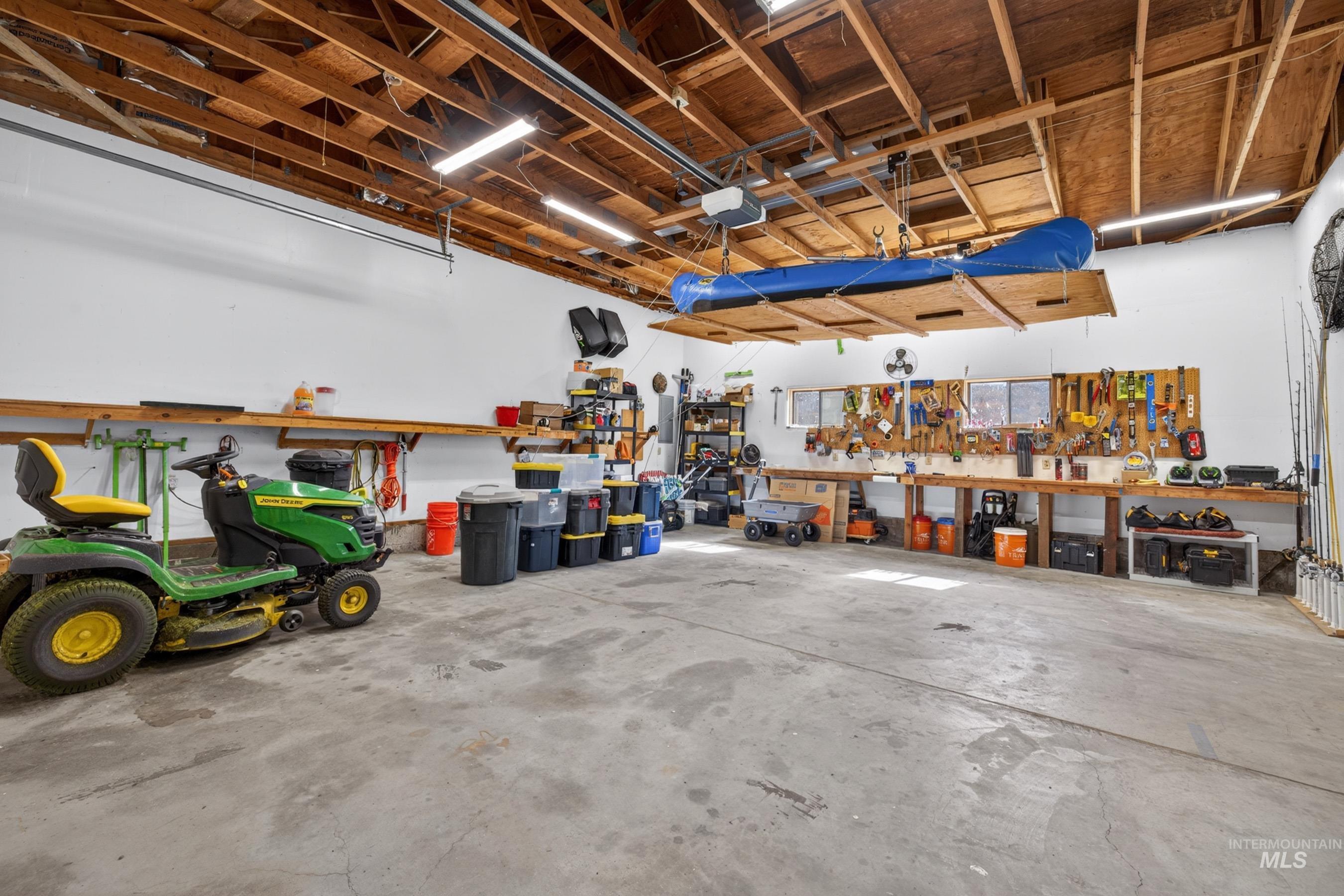 215 Doumecq Road White Bird, ID 83554 - Photo 42 of 50 Spacious garage featuring a concrete floor, exposed wood beam ceiling, white walls, built-in shelving, and multiple fluorescent light fixtures
