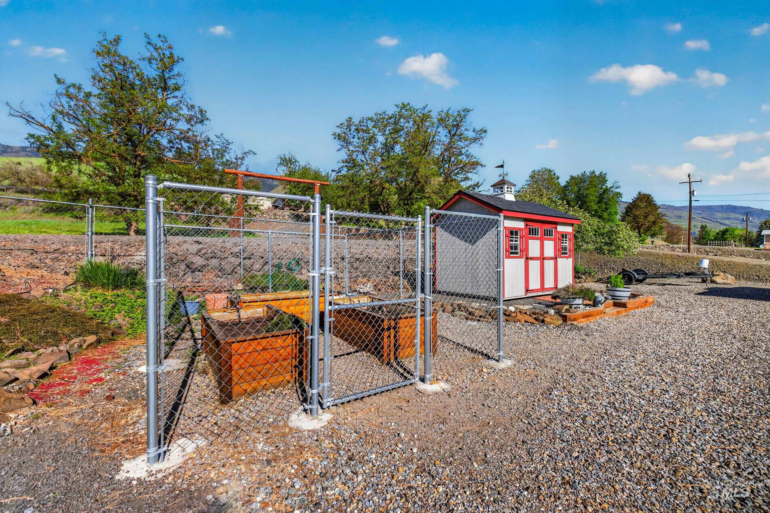 215 Doumecq Road White Bird, ID 83554 - Photo 43 of 50 Red and white utility shed with a cupola and weather vane, featuring an expansive gravel yard and a chain-link fence with gates