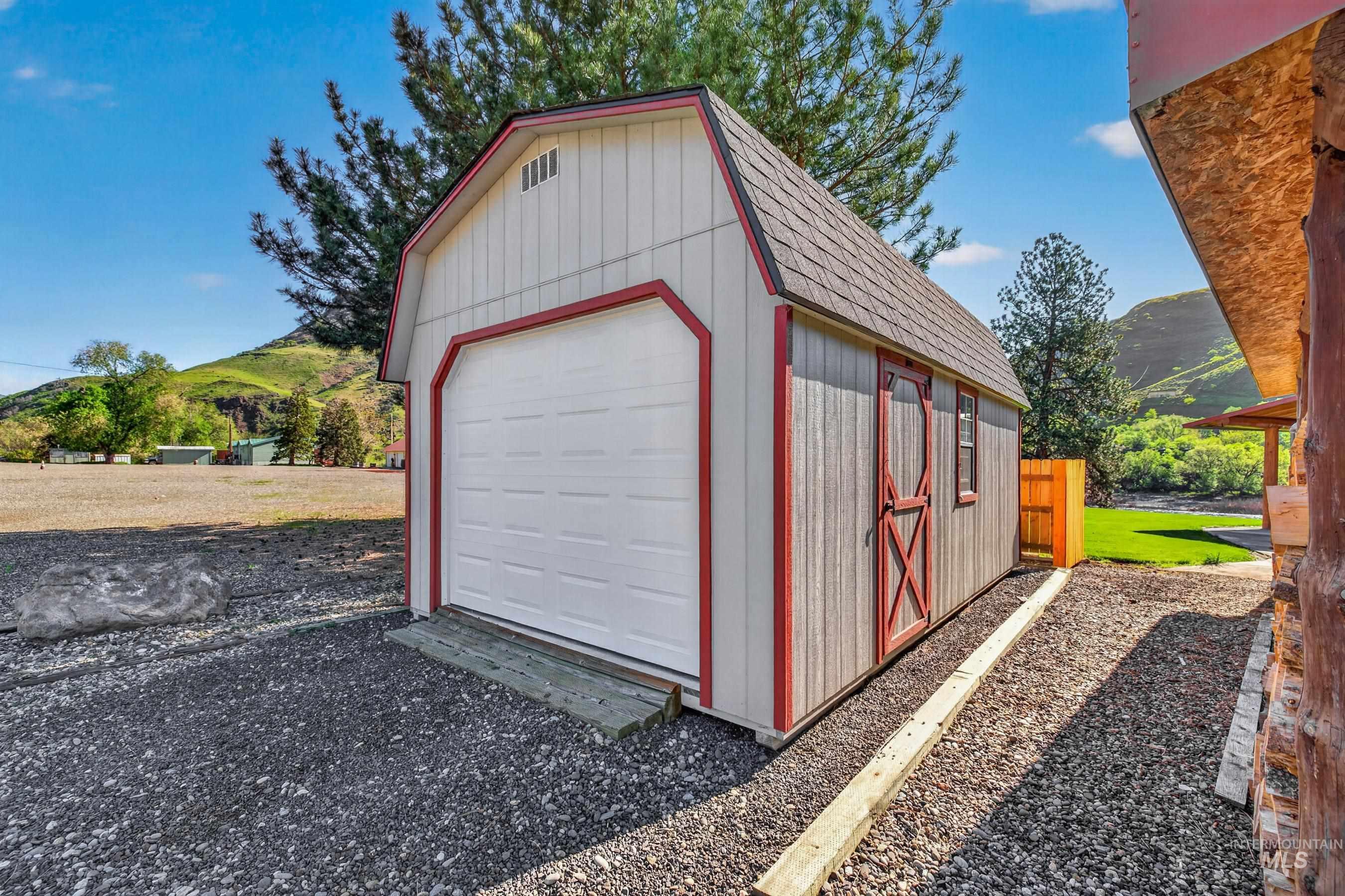 215 Doumecq Road White Bird, ID 83554 - Photo 45 of 50 Barn-style utility building with a roll-up garage door, side entrance, and shingled roof