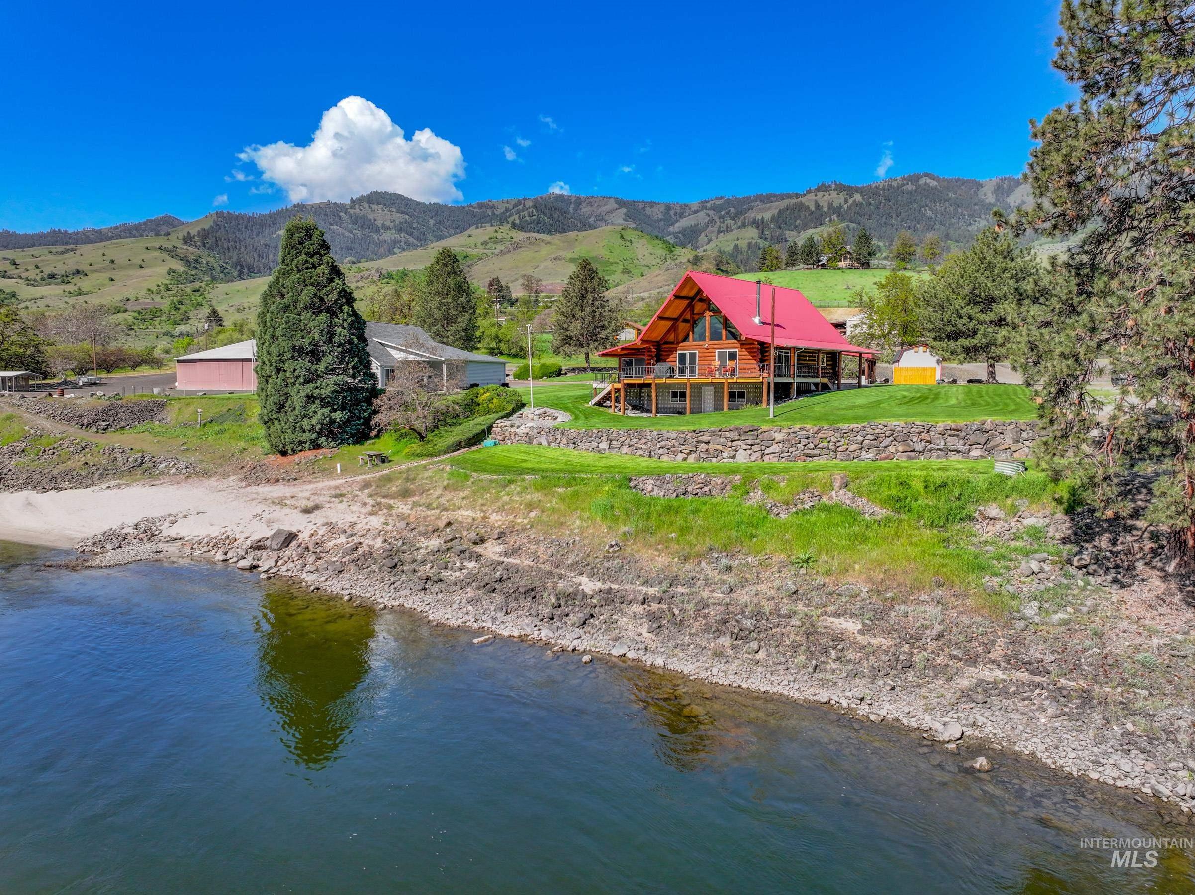215 Doumecq Road White Bird, ID 83554 - Photo 50 of 50 Waterfront log cabin featuring a vibrant red roof, expansive wood deck, and a green lawn