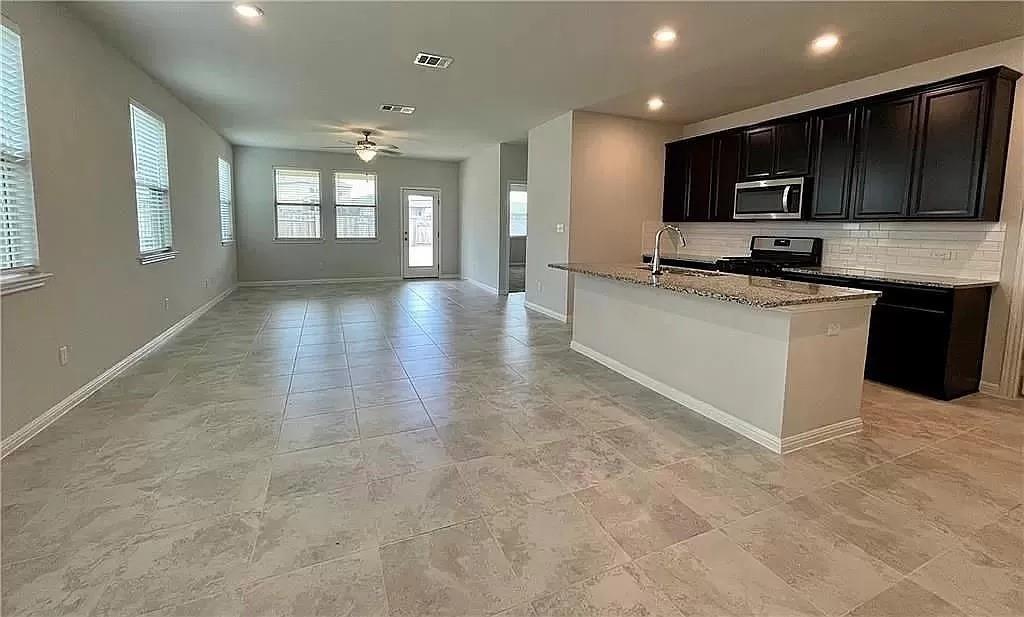 317 Serpens Street Georgetown, TX 78628 - Photo 2 of 13 a large kitchen with stainless steel appliances granite countertop a stove top oven a sink dishwasher a microwave oven and a refrigerator with wooden cabinets