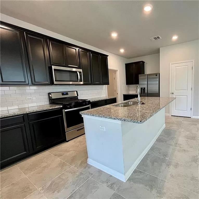 317 Serpens Street Georgetown, TX 78628 - Photo 3 of 13 a kitchen with kitchen island granite countertop stainless steel appliances microwave stove refrigerator and sink