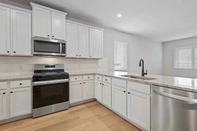 a kitchen that has a lot of white cabinets and stainless steel appliances