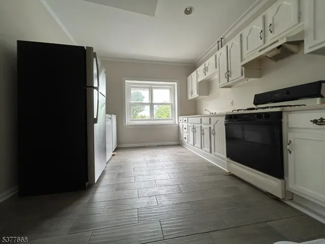 a view of an empty room with wooden floor and a kitchen