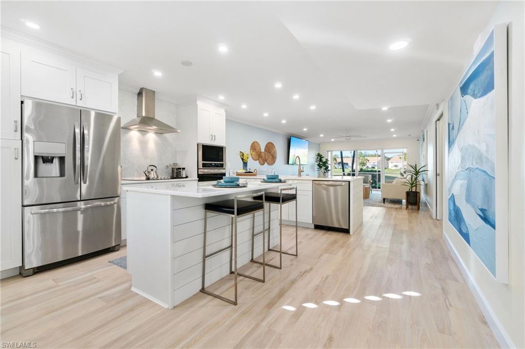 5975 Bloomfield Circle, Unit C108 Naples, FL 34112 - Photo 1 of 50 Kitchen featuring wall chimney exhaust hood, Frigidaire Gallery Appliances, a breakfast bar, stainless steel appliances, white shaker cabinets, and a kitchen island with white marble.