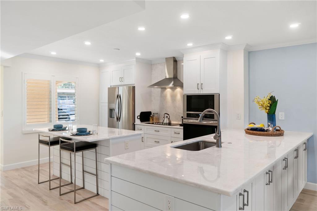 5975 Bloomfield Circle, Unit C108 Naples, FL 34112 - Photo 3 of 50 Kitchen featuring white cabinetry, wall chimney exhaust hood, a large island, and appliances with stainless steel finishes