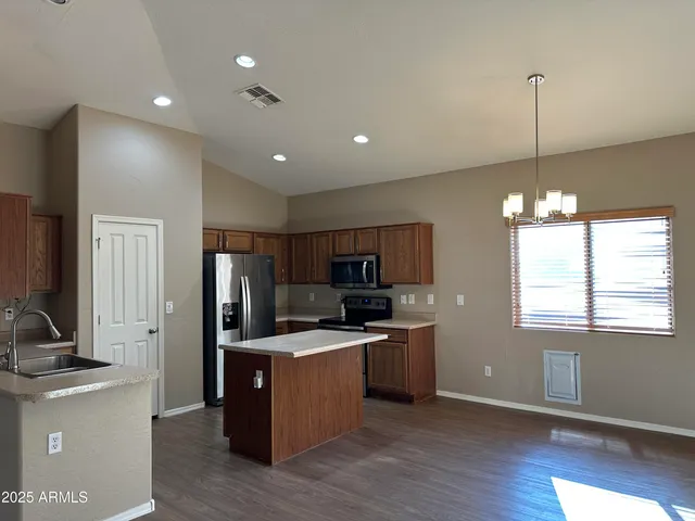 a kitchen with stainless steel appliances granite countertop a refrigerator a sink dishwasher a oven and a dining table with wooden floor