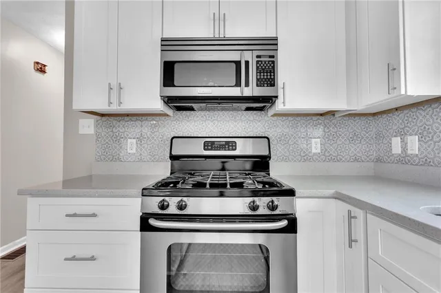 a kitchen with stainless steel appliances granite countertop white cabinets and a stove top oven