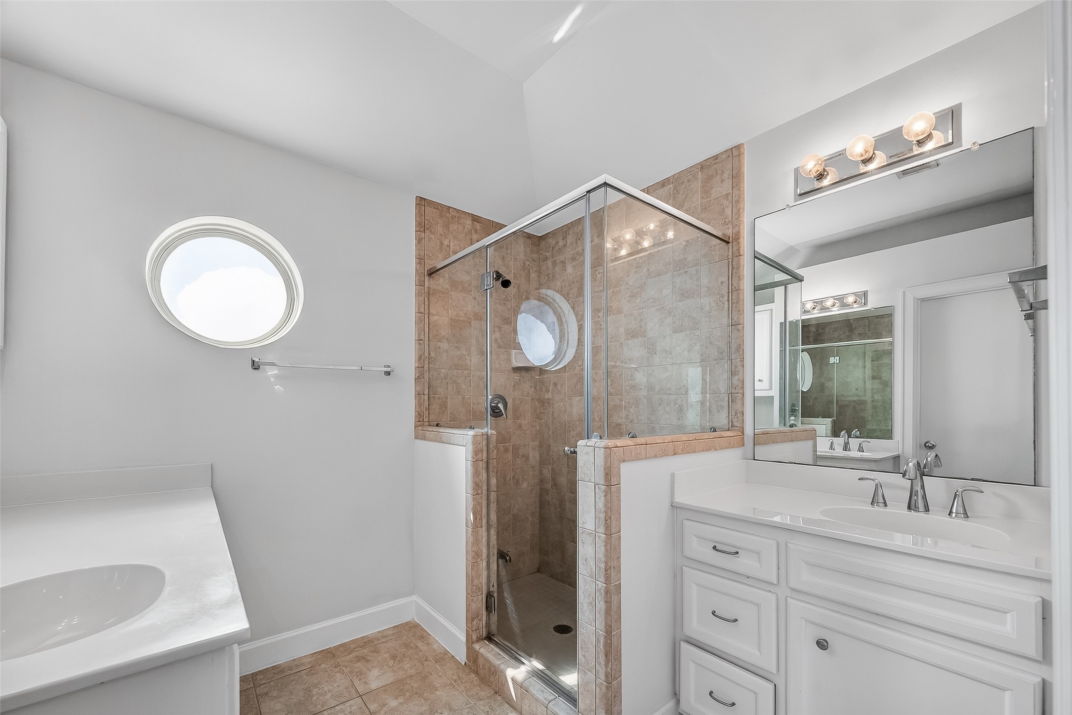 5951 S Loop East, Unit 47 Houston, TX 77033 - Photo 20 of 37 This Primary bathroom features a modern design with a glass-enclosed shower, beige tile accents, and a double vanity. A round window adds natural light, while sleek fixtures enhance the contemporary feel.